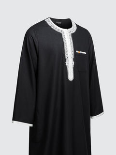 Imaarah Andalus long sleeve Moroccan thobe in black with white embroidery shown at an angled side view highlighting contrast detailing and relaxed fit
