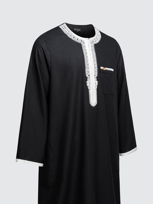 Imaarah Andalus long sleeve Moroccan thobe in black with white embroidery shown at an angled side view highlighting contrast detailing and relaxed fit