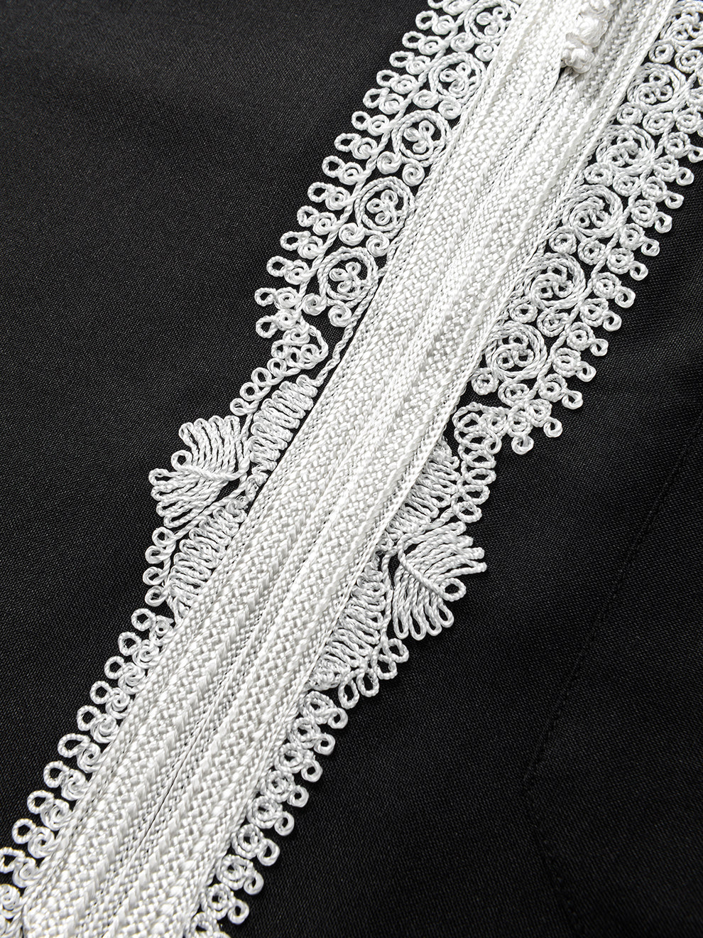 Close-up of white Moroccan embroidery on Imaarah Andalus long sleeve thobe showing detailed stitching and fabric texture on black base